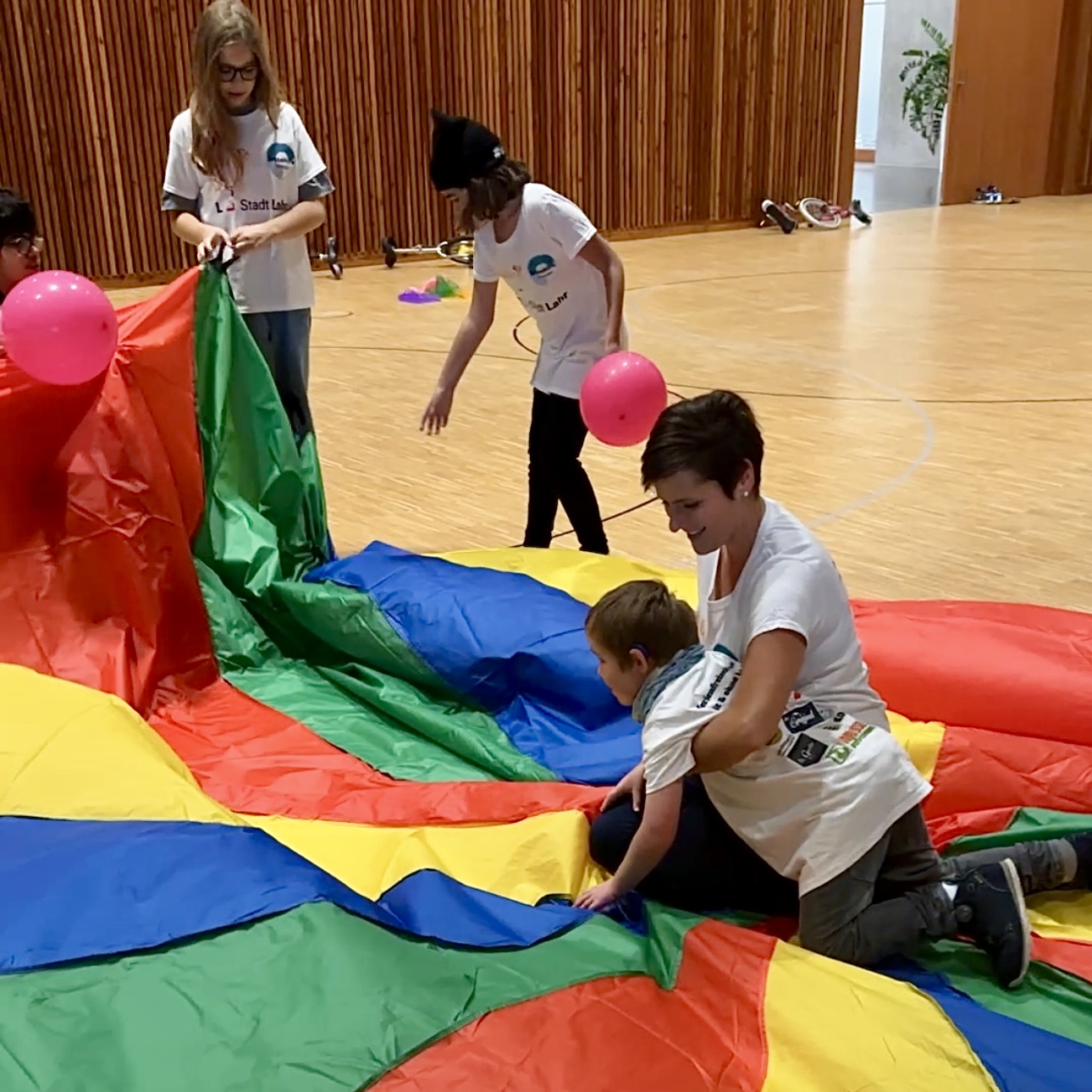 Kinder mit und ohne Handicap spielen gemeinsam mit einem bunten Schwungtuch in der Turnhalle während des inklusiven Ferienprogramms Herbst 2025