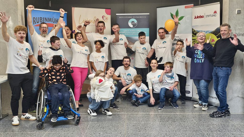 Teilnehmende des inklusiven Ferienprogramms Herbst 2025 stehen vor Sponsoren-Bannern und feiern gemeinsam den erfolgreichen Abschluss